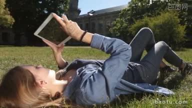 迷人的金发女孩躺在她的绿色草地上触摸板，学习校园特写